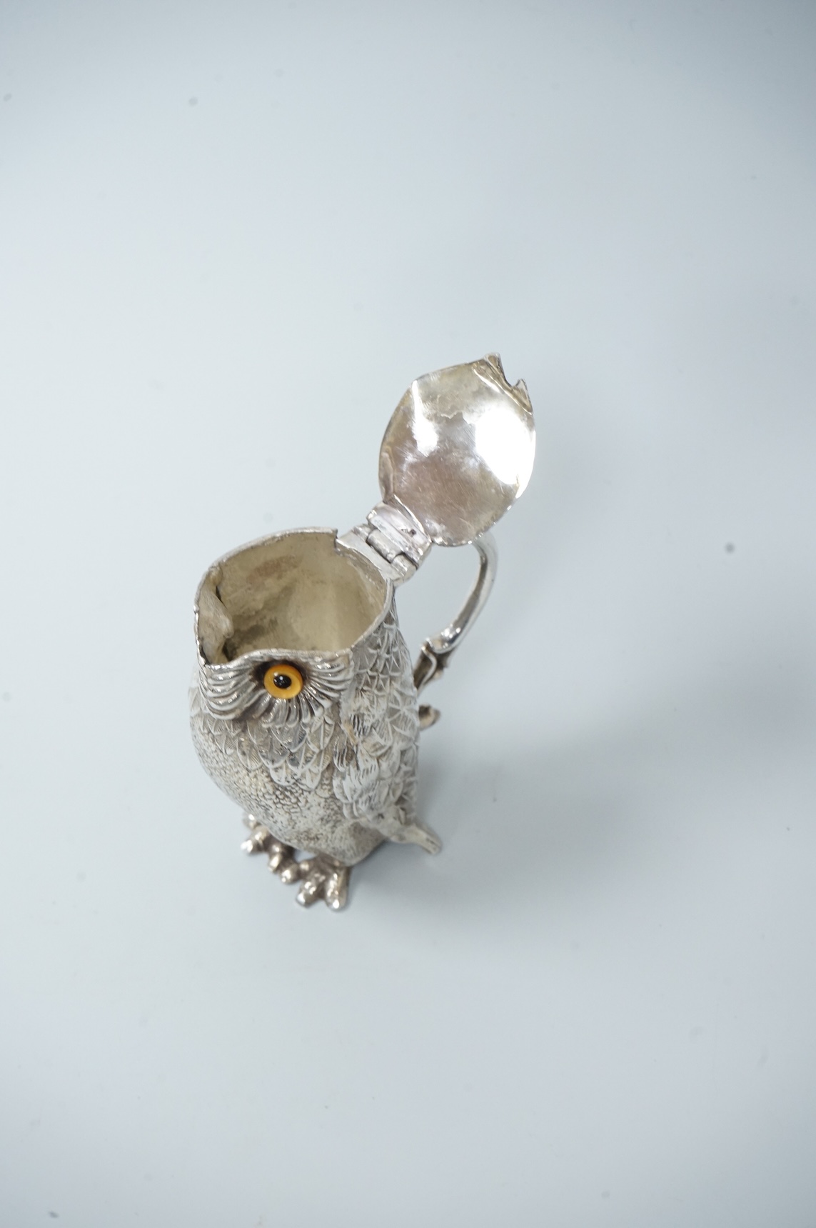 A novelty white metal single handled mustard pot, modelled as a free-standing owl, with hinged cover and textured 'feathers', unmarked, height 95mm.